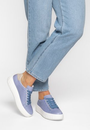 Person wearing light blue jeans and lavender sneakers with thick white soles, standing against a plain white background.
