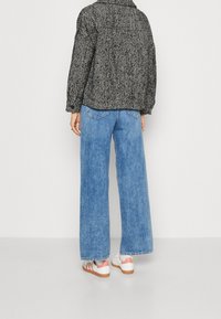 Czarny i biały, paskowany, oversize'owy żakiet w połączeniu z jasnoniebieskimi spodniami o szerokiej nogawce oraz białymi trampkami z różowymi akcentami, widok z tyłu.