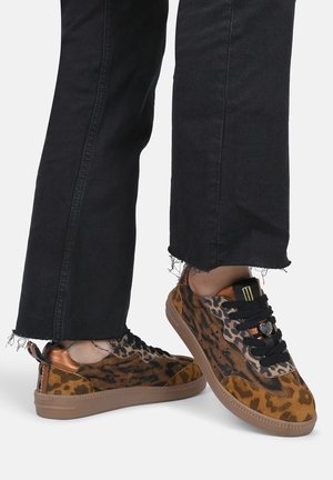 Leopard print sneakers featuring a brown suede upper, black laces, gold accents, and a textured rubber sole. Worn with frayed black jeans.