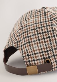 Mütze mit einem braunen, schwarzen und cremefarbenen Hahnentrittmuster, aus Wolle, mit einem braunen Lederriemen und einer Metallschnalle an der Rückseite.