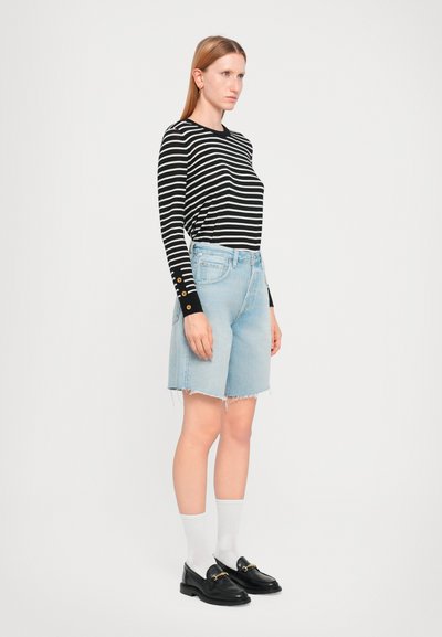 Camicia a righe a maniche lunghe in bianco e nero, pantaloni shorts in denim azzurro chiaro con orli sfilacciati, calzini bianchi e mocassini neri con dettagli dorati.