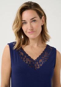 Top senza maniche blu navale con scollatura a V in pizzo ondulato, caratterizzato da un motivo geometrico nel pizzo e da un tessuto morbido e strutturato.