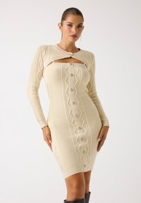 Abito in maglia color crema con maniche lunghe, con un'apertura, chiusura a bottoni e motivi testurizzati. Realizzato in un morbido materiale a coste.