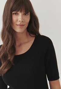 Haut noir à côtes avec des manches courtes et un décolleté large, présentant une finition texturée et une silhouette ajustée.