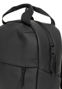 Mochila negra con una textura suave y mate; cuenta con un asa superior y una cremallera con tirador negro, diseñada para la durabilidad y la utilidad.