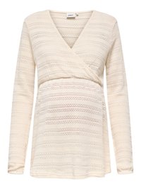 Dolga nosečniška majica kremne barve z V-izrezom in prekrivnim vzorcem ter subtilnimi teksturiranimi vodoravnimi črtami.