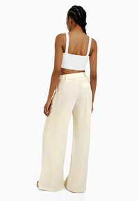 Vit ribbad kort topp kombinerad med högmidjade, vida ljusbeige byxor, med slät tyg och minimalistisk design.