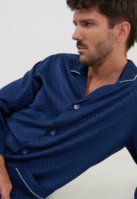 Conjunto de pijama azul marino con un patrón de diamantes, que cuenta con una parte delantera de botones, cuello con muesca y ribete blanco a lo largo del cuello y el bolsillo.