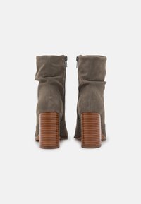 Botas de tobillo de ante gris con un diseño arrugado y tacones de madera acanalados, que incluyen cremalleras en la parte de atrás para un fácil uso.