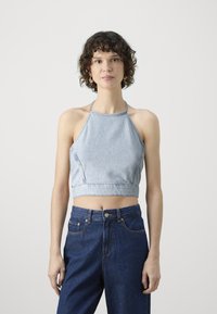 Top corto a halter in denim azzurro chiaro con vita aderente, caratterizzato da cuciture diagonali e spalline sottili, abbinato a jeans scuri a vita alta.