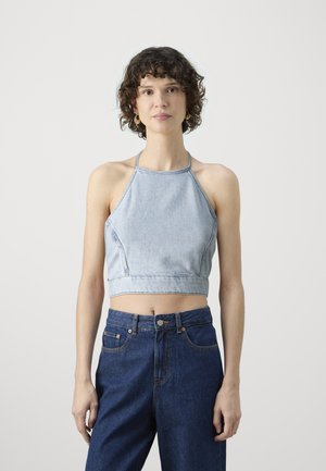 Lyseblå denim halterneck crop top med tettsittende liv, med diagonale sømmer og tynne stropper, kombinert med høyt livet mørkeblå jeans.
