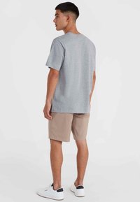 Sivý tričko s krátkym rukávom, vyrobené z mäkkej tkaniny, v kombinácii so svetlo béžovými šortkami. Model má na sebe biele tenisky s čiernymi detailmi.