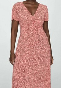 Vestido floral rojo con mangas cortas, escote en V y cintura ajustada. La tela presenta un patrón texturizado de puntos de color crema.