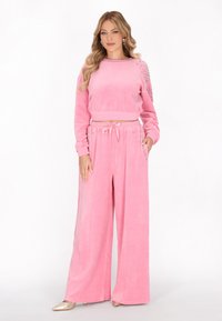Set di abbigliamento in velour rosa composto da una felpa corta con dettagli borchiati sulle maniche e pantaloni a gamba larga con vita regolabile.