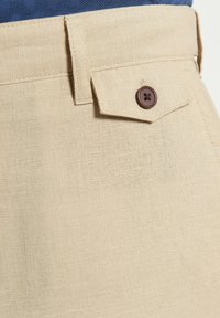 Pantaloni in lino beige realizzati con un tessuto testurizzato, vita aderente e una tasca a patta con un accento di bottone marrone.