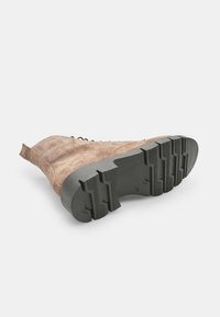 Bottine en suede marron avec un dessus texturé, un design à lacets et une semelle en caoutchouc noir robuste avec des rainures profondes pour une meilleure traction.