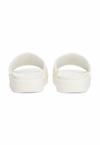 Sandalias blancas de pala plana con una parte superior de textura suave, correas redondeadas y una suela de plataforma gruesa. Nombre de la marca grabado en el costado.