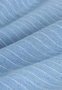 Tissu en denim bleu clair avec une couture blanche diagonale et une texture de tissage visible en plis doux.