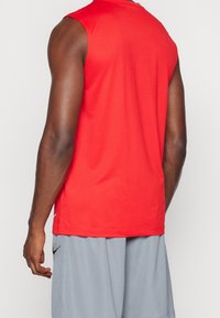 T-shirt de sport rouge sans manches en tissu lisse et léger. Comprend un col rond et un design simple avec des accents minimes.