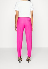 Fuchsiové kalhoty na míru se slim fit střihem, jednou zadní kapsou a hladkou texturou látky. V kombinaci s jednoduchým bílým tričkem a černými sandály.