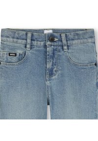 Jeans de mezclilla azul claro con corte recto, que presentan un cierre de botón negro y bolsillos cosidos. Logo de BOSS visible en la parte delantera.