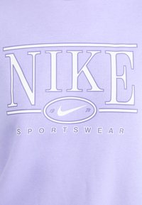 Sweatshirt Nike violet avec un logo blanc bien en vue portant les inscriptions "NIKE", "1972" et "SPORTSWEAR" en typographie audacieuse et épurée. Texture douce.