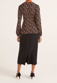 Långärmad topp med ett mönster av bruna, svarta och orangea löv; kombinerad med en svart kjol med en bakslits och högklackade skor.