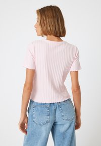 Rosa ribbet strik top med korte ærmer og bølgede kanter, tætsiddende stil og rund halsudskæring. Båret med lyseblå jeans med høj talje.