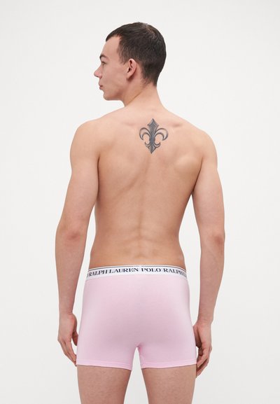 Rózsaszín pamut nadrág elasztikus derékkal, rajta a "POLO RALPH LAUREN" felirattal. A modellen tetoválás látható a hátának felső részén.