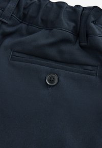 Marineblauwe broek met een gladde textuur, voorzien van een elastische tailleband, knoopsluiting aan de voorkant en een achterzak met een gestikte detail.