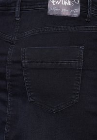 Jeans en denim noir avec une poche arrière visible, présentant des détails de couture subtils et une étiquette indiquant "Nouvelles Lignes" et "Cecil."
