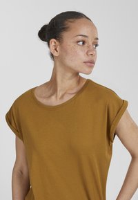 Senapsgul kortärmad t-shirt med bred rund halsringning och avslappnad passform. Mjukt tyg med en slät textur; inga synliga mönster eller detaljer.