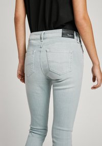 Vaqueros de denim gris claro con un diseño ajustado. Incluye bolsillos traseros y una etiqueta de marca negra en la cintura.