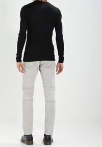 Musta, ribbineuloksinen pitkähihainen paita yhdistetty vaaleanharmaisiin, kapealahkeisiin farkkuihin, joissa on polvikoristukset; asu viimeistelty mustilla kengillä.