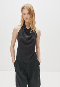 Sort halterneck-top med draperet cowl-udskæring, lavet af et glat stof. Ingen synlige mønstre; modellen har løse, mørke bukser med striber på.