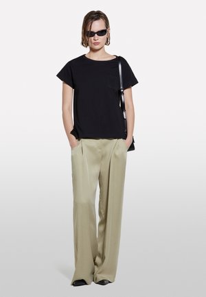 T-shirt nera in cotone a maniche corte con tasca, abbinata a pantaloni beige a vita alta e gamba larga. Occhiali da sole neri e borsa completano il look.