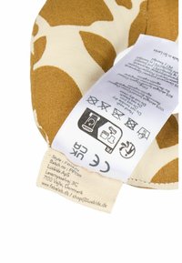 Țesătură maro și crem cu un imprimeu de girafă. Conține etichete de întreținere, inclusiv instrucțiuni de spălare, marcaj CE și detalii despre brand pe etichetă.