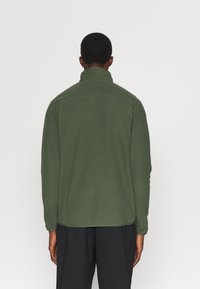 Grüne Fleecejacke mit hohem Kragen, langen Ärmeln und glatter Textur, ausgestattet mit einem geraden Saum und minimalen Nähten auf der Rückseite.