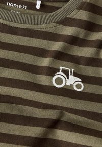 Zielono-brązowa w prążki tkanina z małym białym haftowanym traktorem w pobliżu dekoltu dziecięcej koszulki.