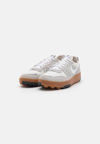 Scarpe da ginnastica grigio chiaro con tomaia in suede e mesh, lacci bianchi e suola in gomma color caramello con tacchetti neri per la trazione.