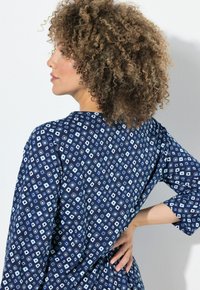 Abito blu navy con un motivo geometrico a diamante in bianco e azzurro chiaro. Maniche a tre quarti e una vestibilità ampia e rilassata.