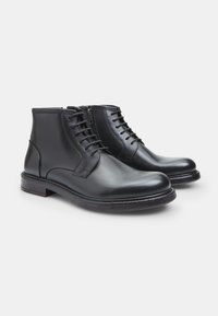 Botas de tobillo de cuero negro con una textura suave, diseño con cordones y cremallera lateral. Presentan una punta redondeada y un resistente tacón de madera.