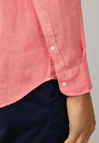 Roze linnen overhemd met een knoopmanchet en tabdetail. Kenmerkt zich door een afgeronde zoom en een zachte textuur, gecombineerd met donkerblauwe broek.