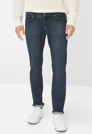 Donkerblauwe denimjeans met een slim fit, lichte stretch, vijf-pocket ontwerp en omgeslagen zoom, gecombineerd met witte sneakers.
