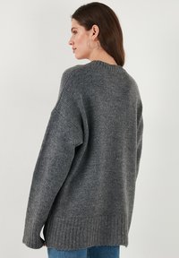 Sweatshirt gris surdimensionné avec ourlet côtelé, texture douce et manches larges. La vue montre le détail du dos, mettant en valeur le motif de tricot et la coupe décontractée.