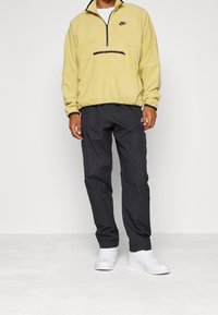 Gul fleece-tröja med kvartslång dragkedja och svarta detaljer, ihop med svarta cargobyxor och vita sneakers. Enkel design och textur.