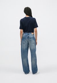 Μπλε σκούρο πουκάμισο με κοντά μανίκια, σε συνδυασμό με άνετο ανοιχτό μπλε τζιν παντελόνι. Ορατές πίσω τσέπες και ετικέτα κολλώματος στη μέση.