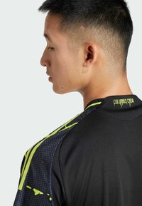 Schwarzes Sporttrikot mit gelben Akzenten und einem gepunkteten Muster auf den Schultern. Mit dem "Columbus Crew"-Logo am Kragen.
