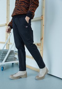 Black tapered pants with elastic waistband, featuring a small Champion logo. Paired with high-ankle beige boots with textured soles.