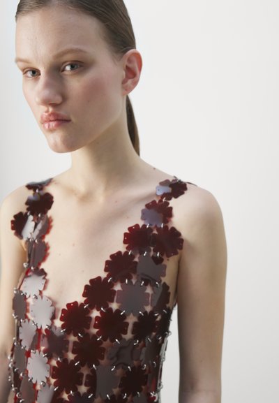 A burgundy floral dress made of translucent material, featuring flower shapes with metallic accents and a deep V-neckline.